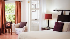 Une chambre d’hôtel avec un lit, une chaise, une table de chevet, une lampe et une fenêtre avec des rideaux.