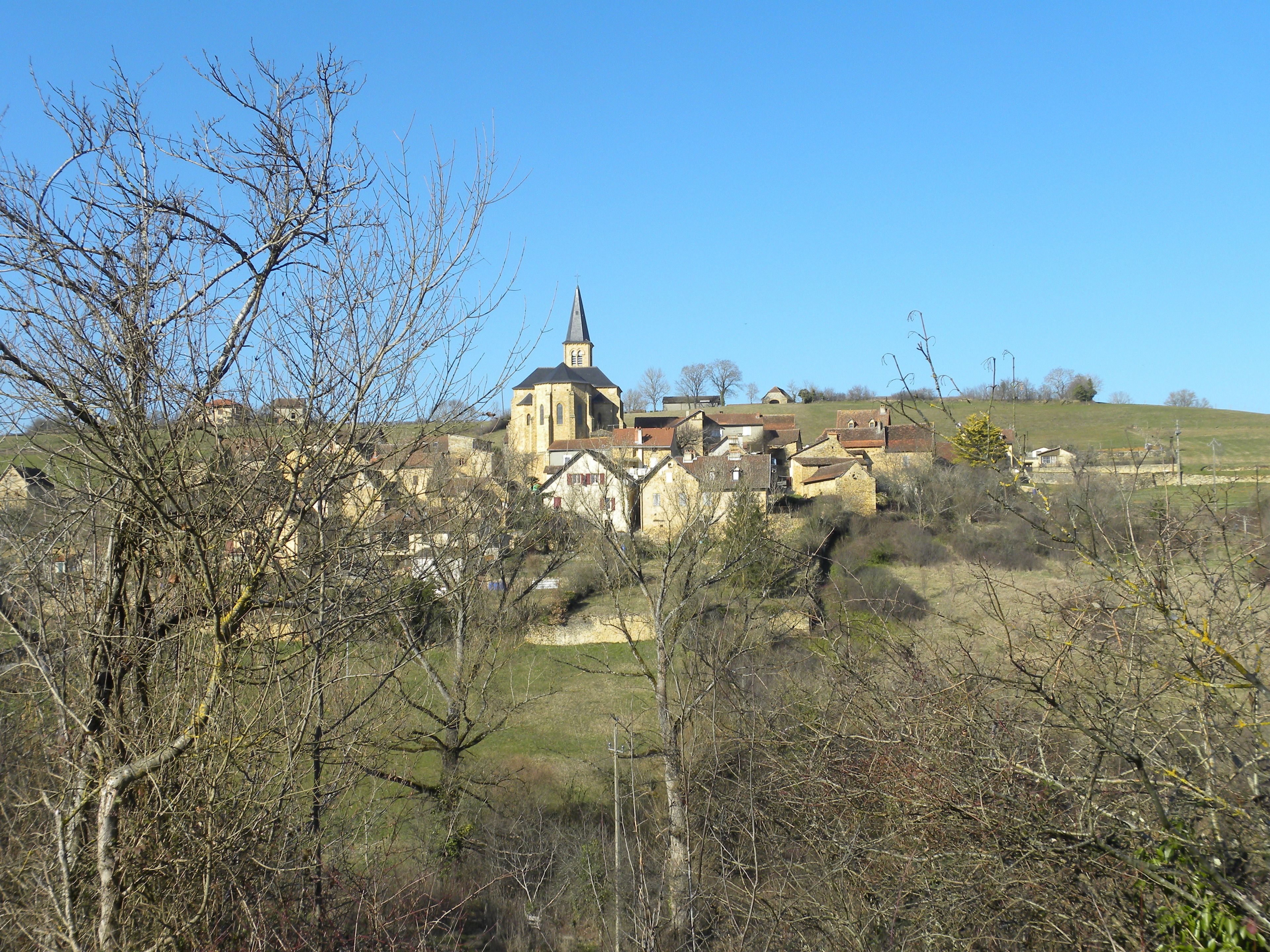 A historic church with a tall steeple, surrounded by traditional stone buildings and a hilly landscape.