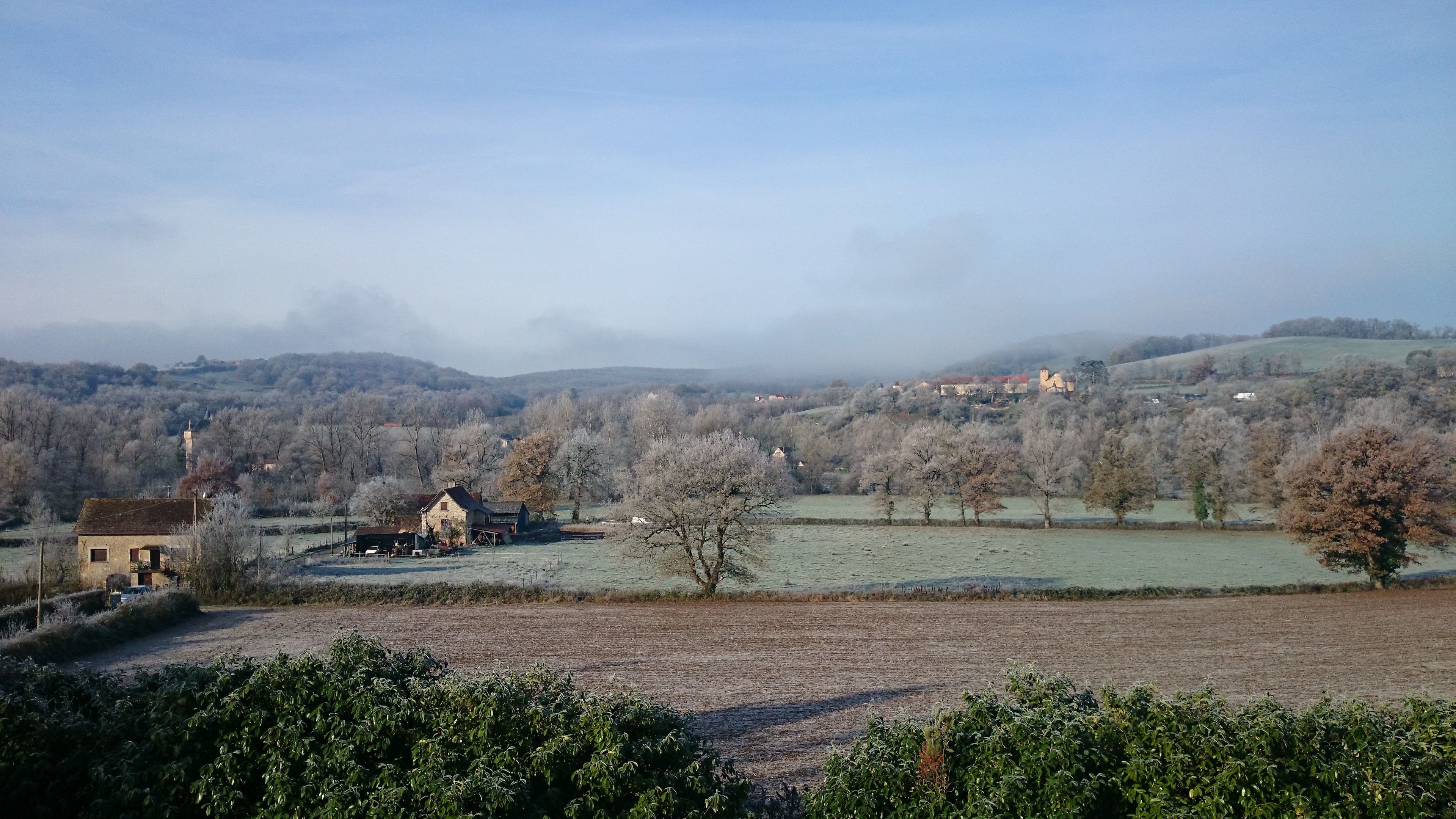Un paysage rural avec une ferme, des champs et des collines à l’horizon.