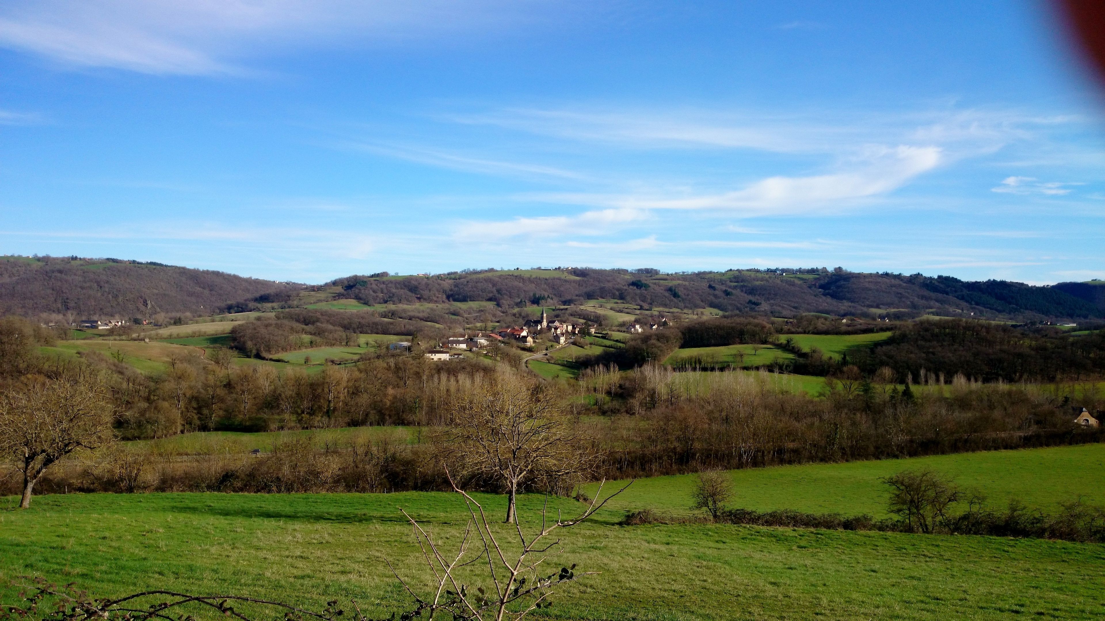 Ländliche Landschaft mit sanften Hügeln, einem kleinen Dorf und einer Kirche.