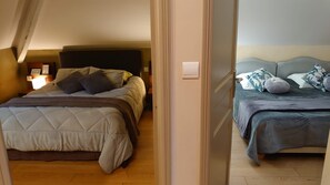 Une chambre avec deux lits, un plancher en bois et une porte visible donnant sur une autre pièce.