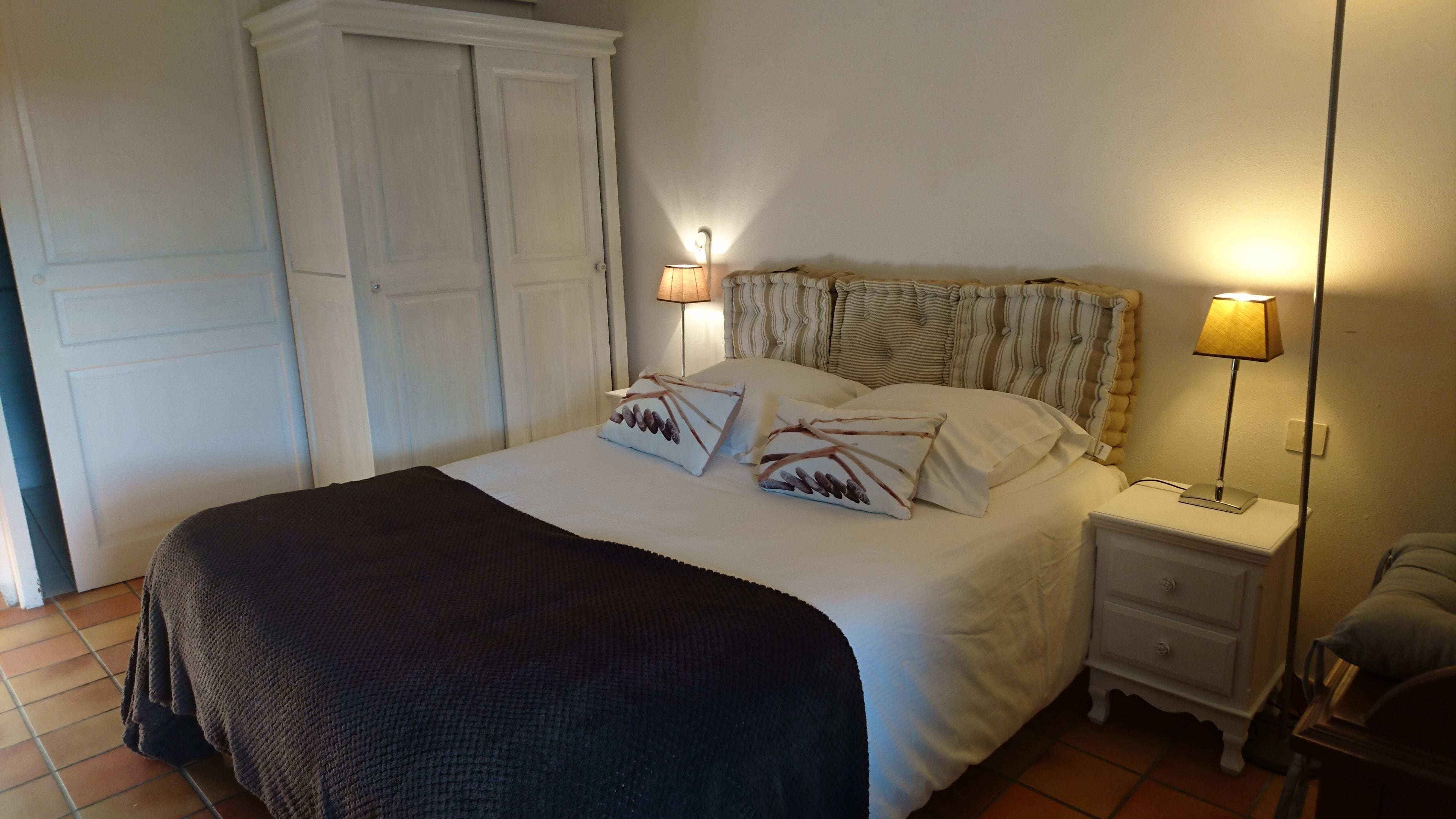 A neatly made bed with pillows, a bedside table with a lamp, and a wardrobe.