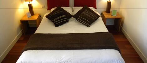 A neatly made bed with two pillows, a red headboard, and two bedside lamps.