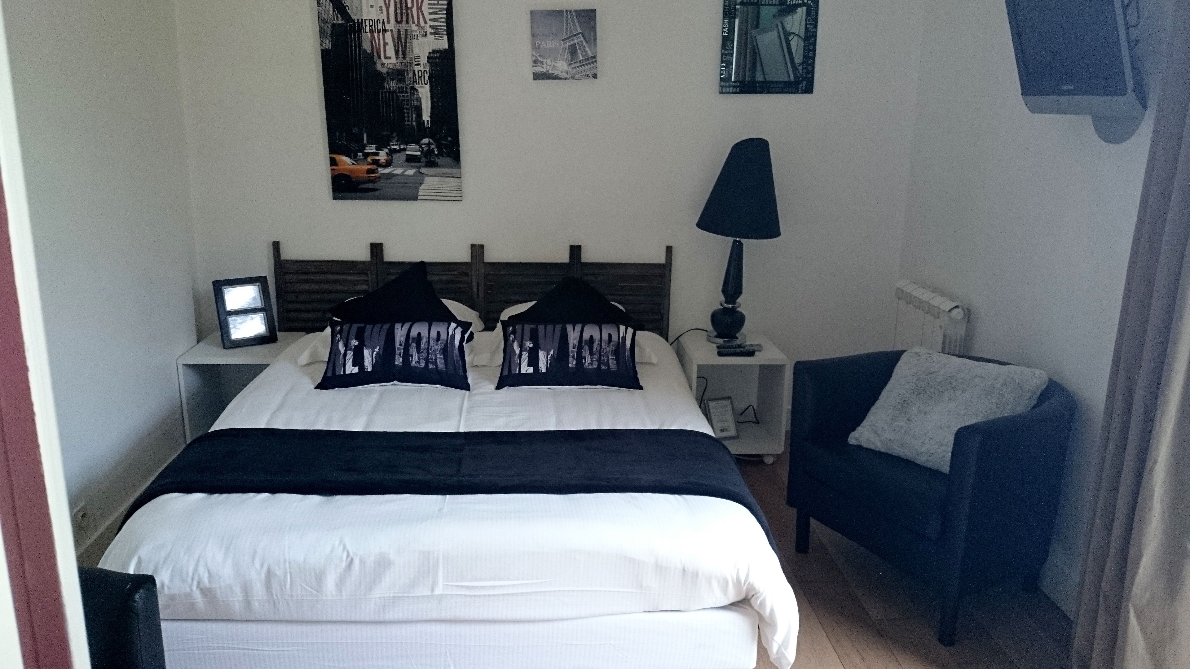 A hotel room with a bed, a nightstand, a lamp, a chair, and wall art.
