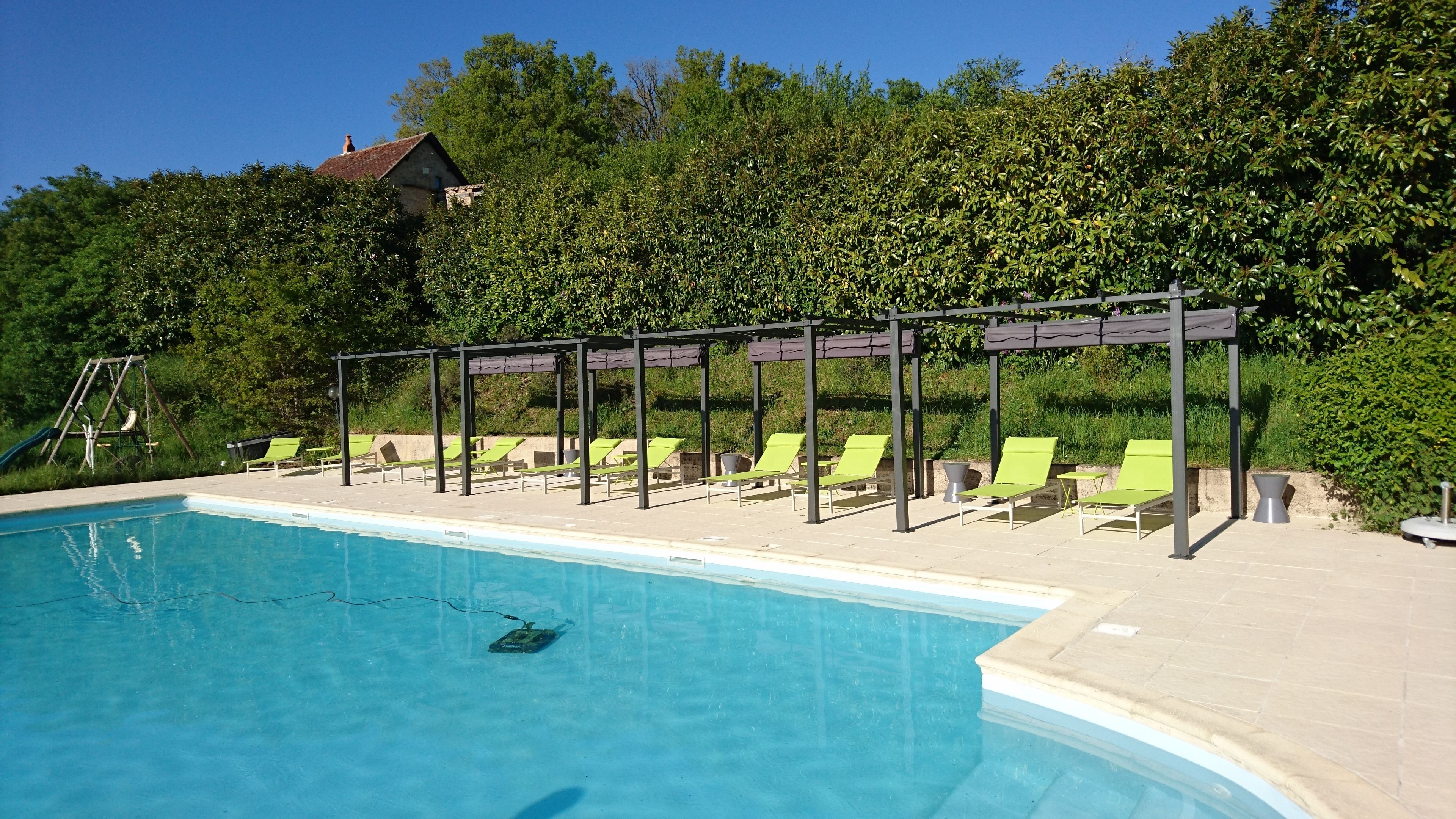 Une piscine entourée de chaises longues vertes et agrémentée d’une pergola.