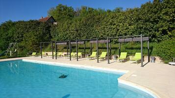 Une piscine entourée de chaises longues vertes et agrémentée d’une pergola.