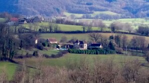 Un paysage rural avec plusieurs bâtiments, dont une grande maison à toit rouge et des constructions plus petites, le tout entouré de champs et d’arbres.