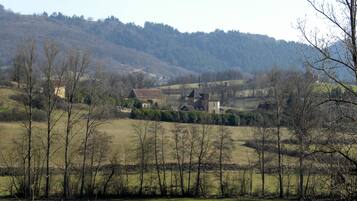 Paesaggio rurale con un gruppo di edifici, tra cui una casa in evidenza con un tetto spiovente, circondata da campi aperti e alberi sparsi.
