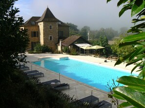 A swimming pool with lounge chairs, a stone building with a tower, and umbrellas. - Hotel La Bastie D Urfe (Naussac)
