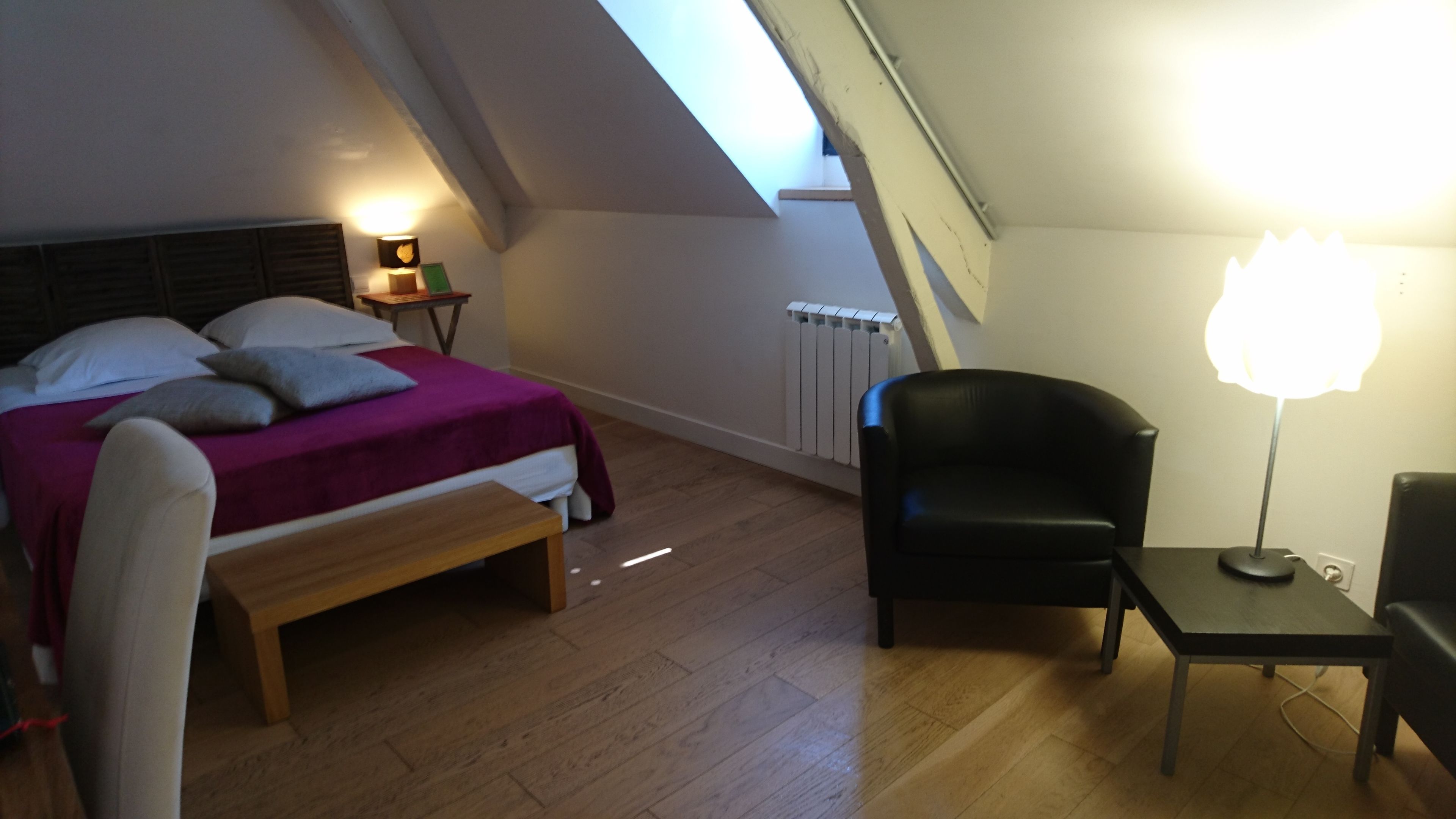 Un dormitorio con cama, una silla, una mesa y una lámpara.