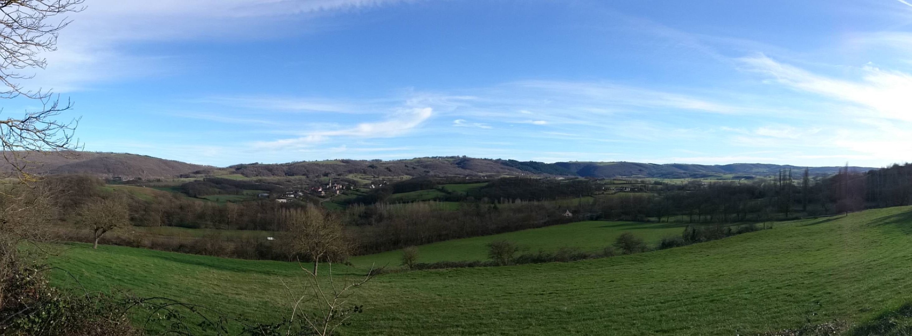 Paisaje rural con colinas onduladas, un pequeño pueblo y cielo despejado.