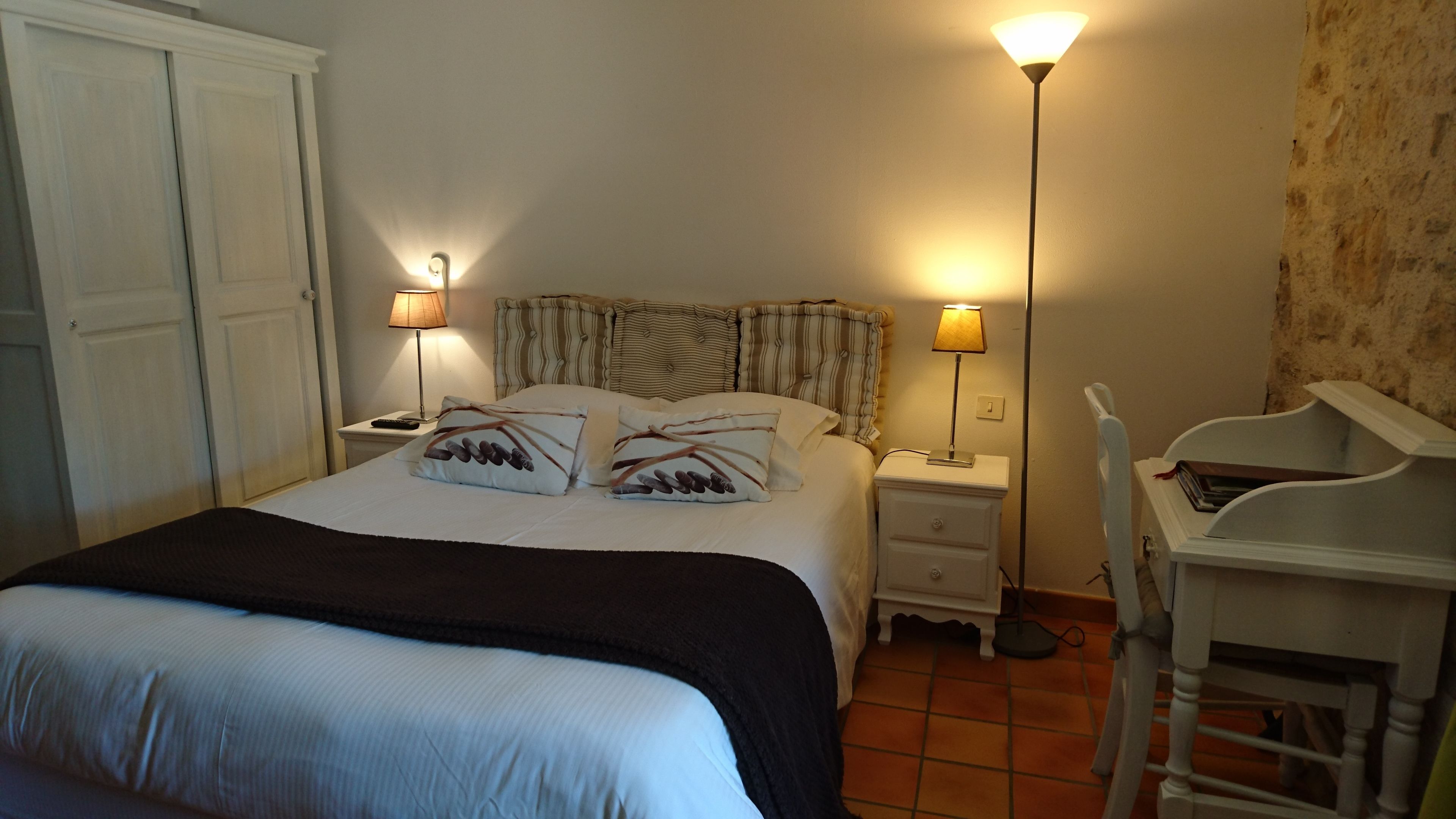 A bedroom with a bed, two bedside tables, a nightstand, a desk, and a chair.