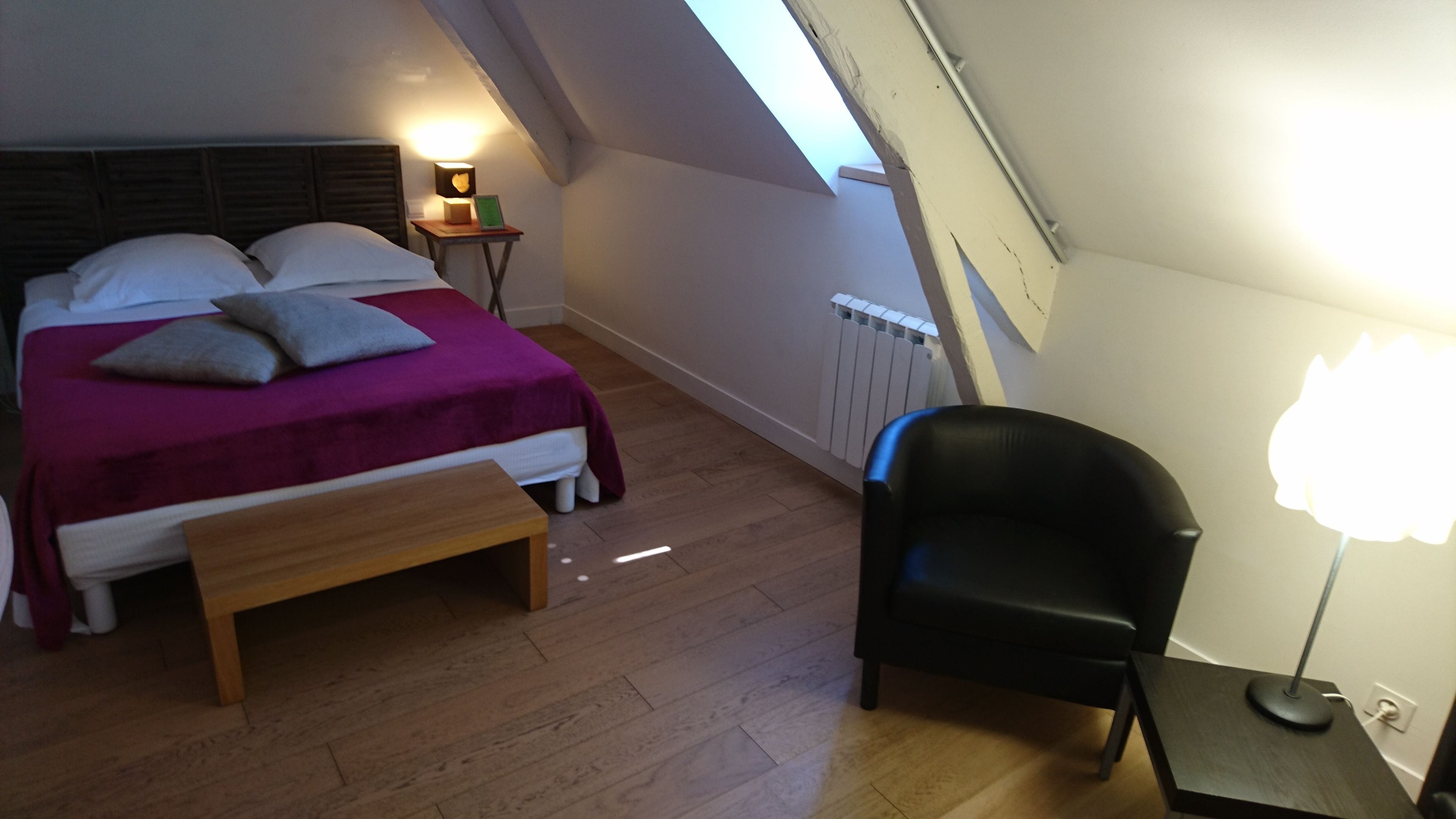 A bedroom with a bed, a bedside table with a lamp, a chair, and a radiator.