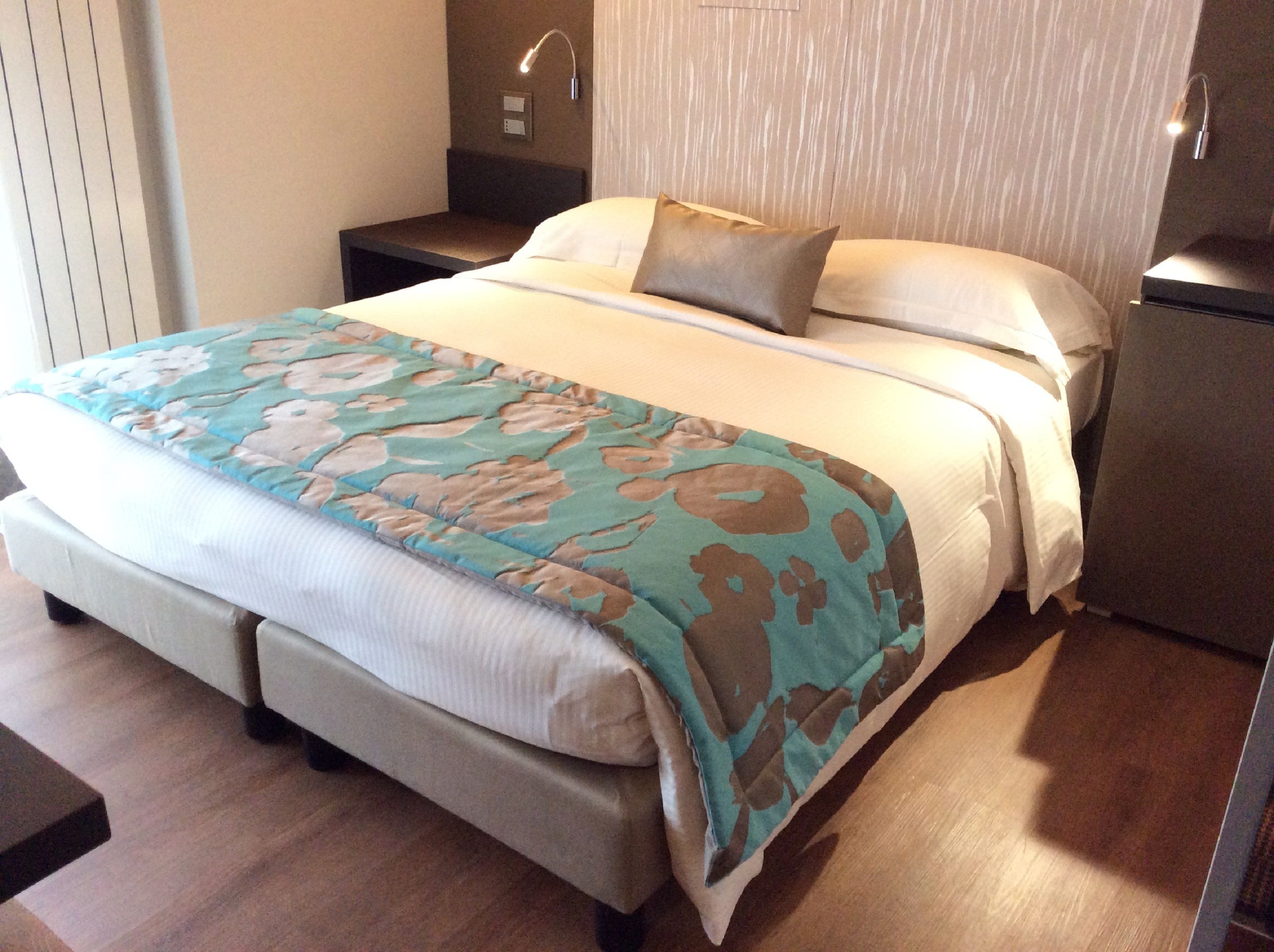 A neatly made bed with a patterned bedspread, a bedside table, and a nightstand.