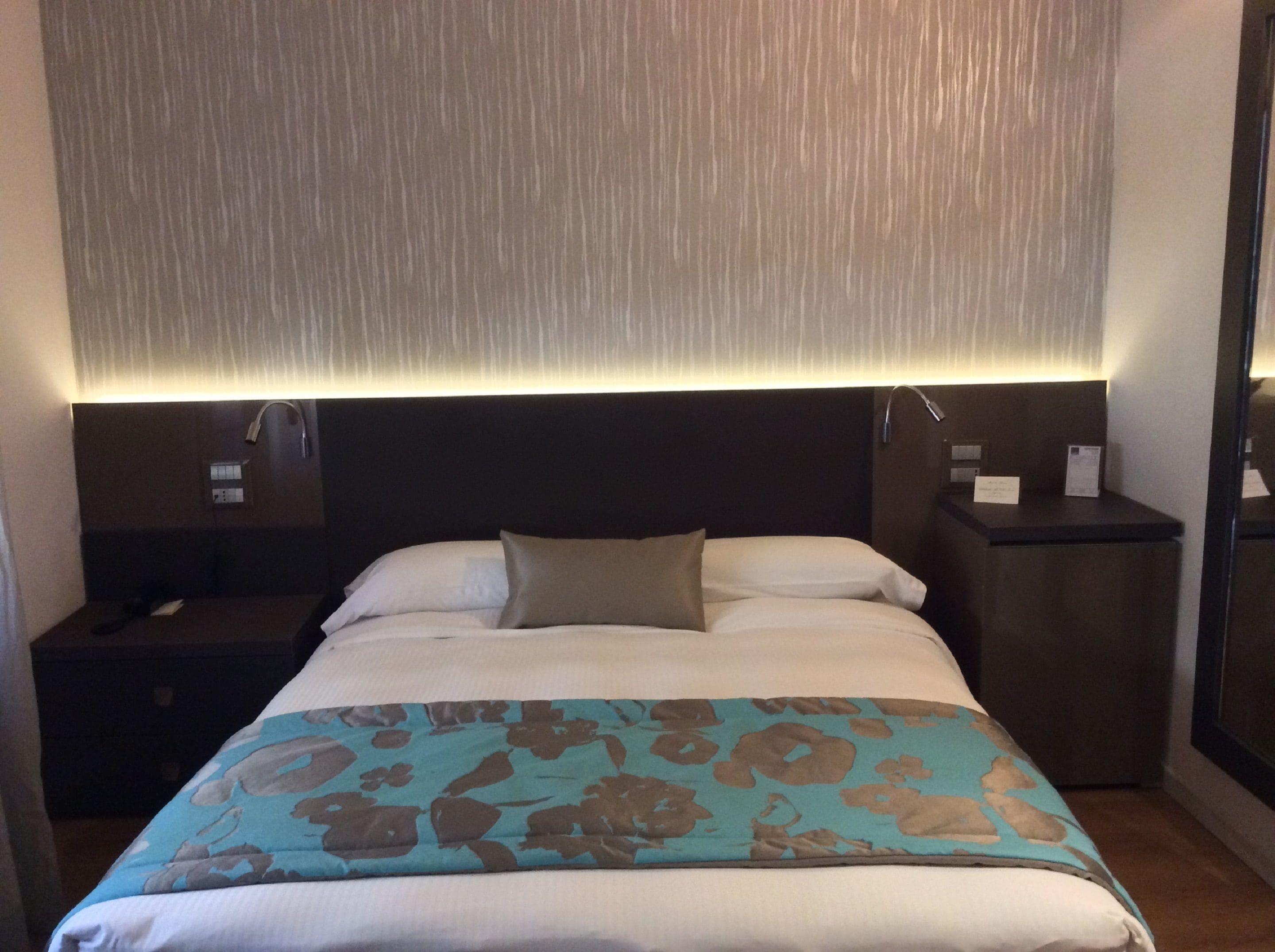 Une chambre d’hôtel avec un lit, une table de chevet, une lampe et un miroir.