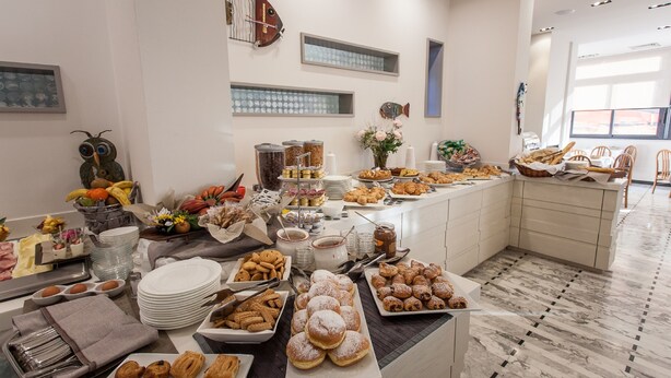 A buffet with various food items and utensils, a fish decoration on the wall, and a tiled floor. - Hotel Ariston (Varazze)