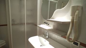 Un bagno con box doccia in vetro, un lavandino bianco con specchio sopra e un asciugacapelli fissato alla parete.