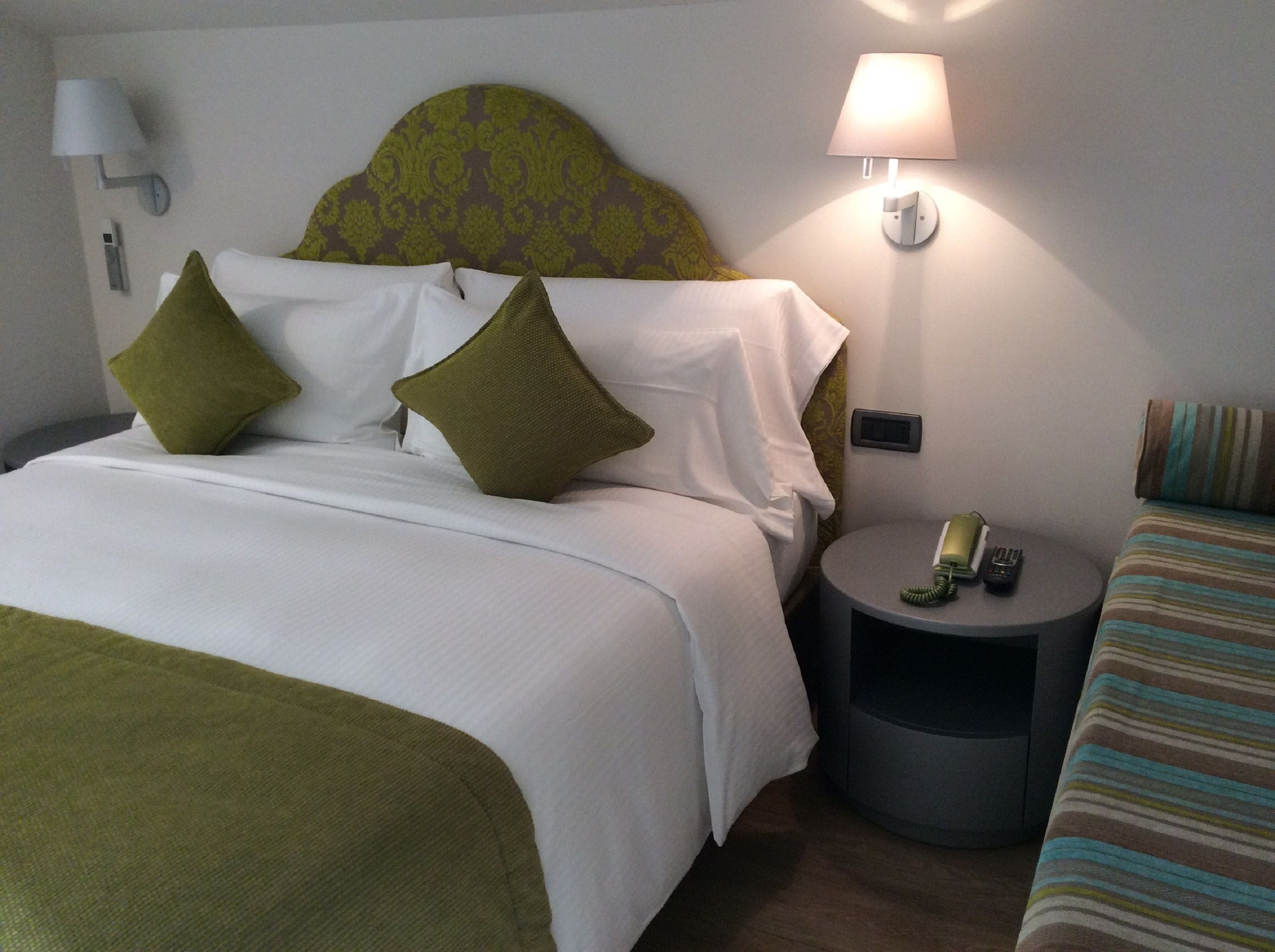 A hotel room with a bed, a nightstand with a lamp, a phone, and a striped bedspread.