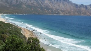 A coastal landscape with a beach, clear blue sea, and a mountain range in the background. - 185 on Beach Boutique Suites and Apartments (Cape Town)
