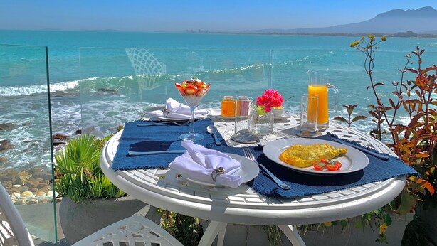 A table set with breakfast items and drinks on a balcony overlooking the sea. - 185 on Beach Boutique Suites and Apartments (Cape Town)