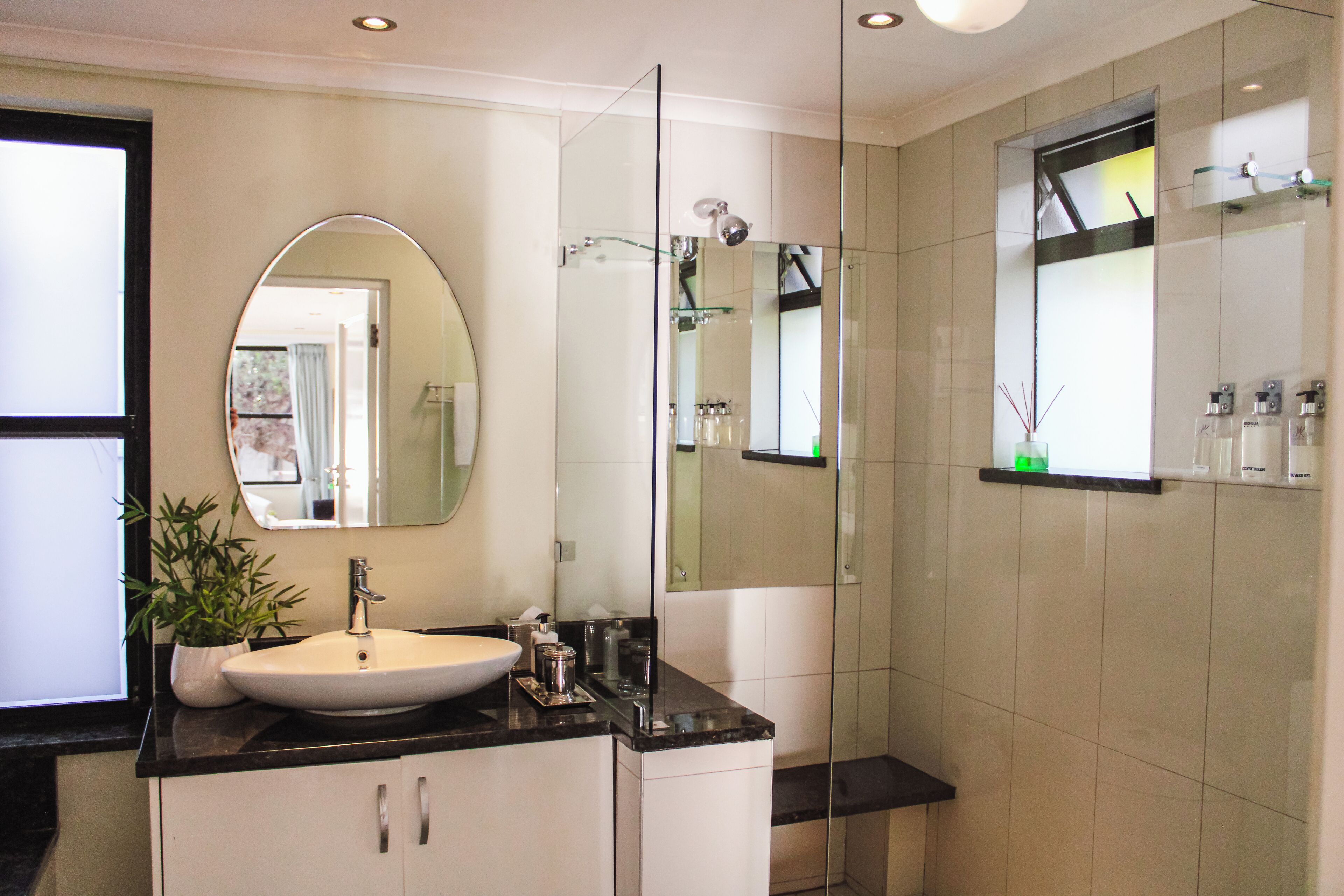 Un baño moderno con un lavamanos blanco, un espejo grande y una cabina de ducha con paredes de vidrio.