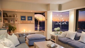 A modern living room with a fireplace, comfortable seating, and a large window with a cityscape view. - 185 on Beach Boutique Suites and Apartments (Cape Town)
