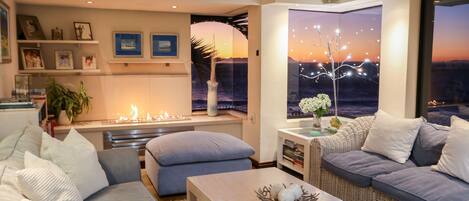 A modern living room with a fireplace, comfortable seating, and a large window with a cityscape view.