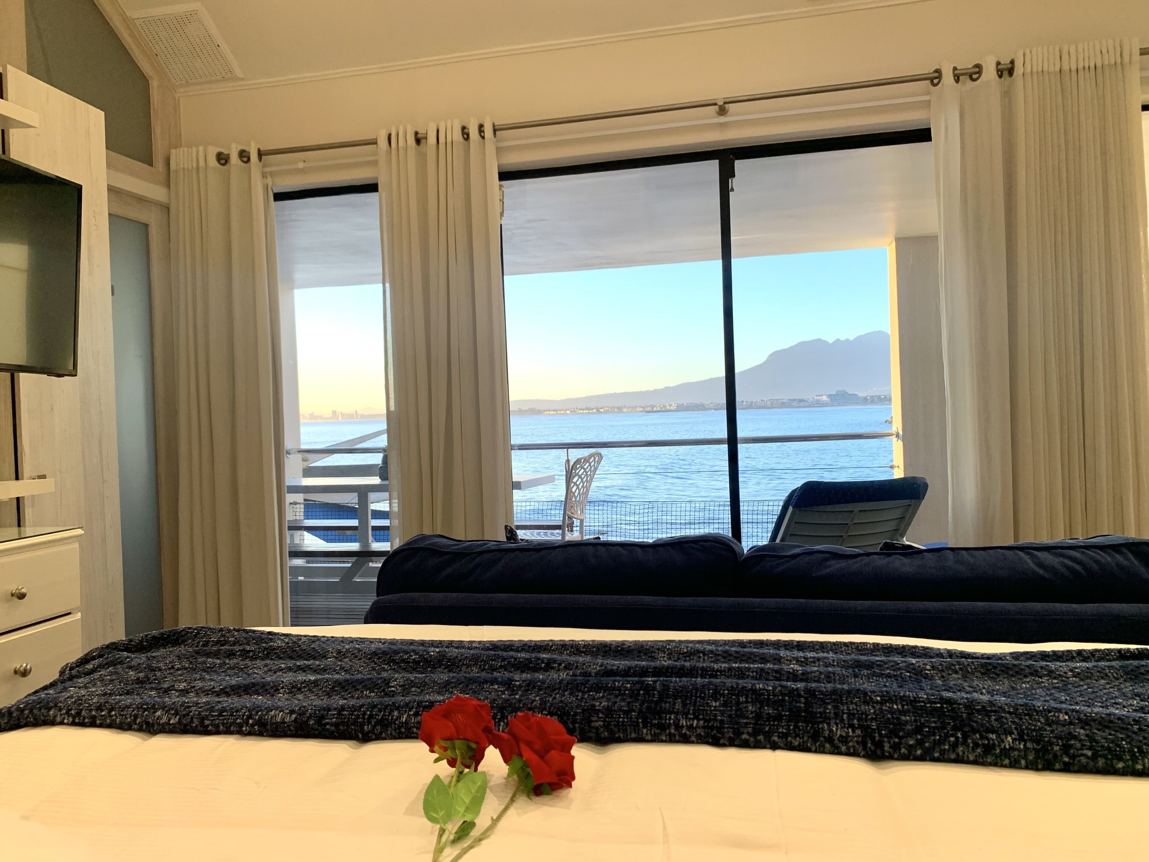 A hotel room with a bed, a view of the sea, and a balcony with a chair.