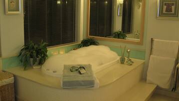 Bathroom features a large bathtub, mirror, and window with blinds, along with a towel rack and toiletries.