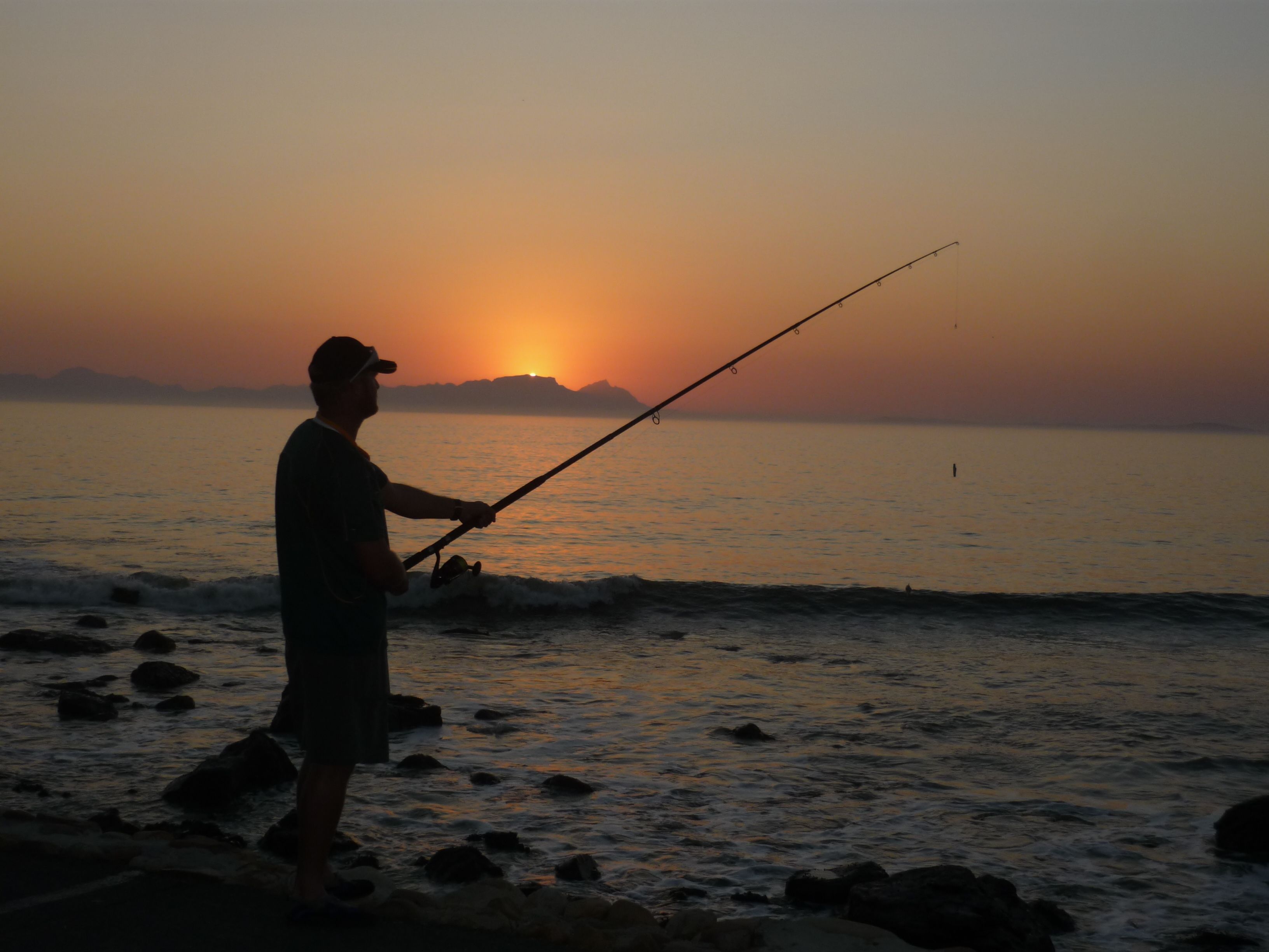 A person fishing by the sea during sunset.