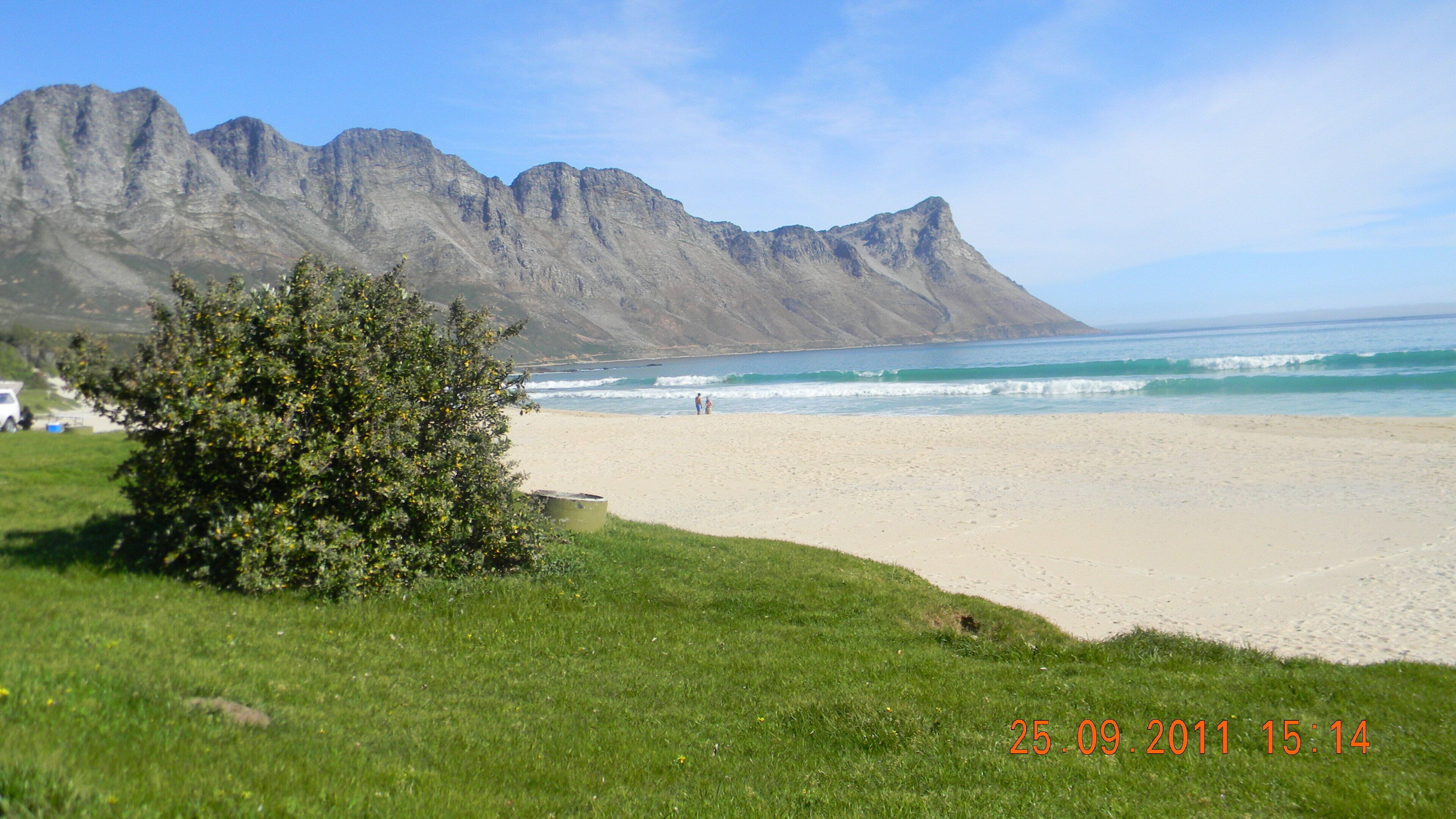 A beach with mountains in the background, a clear sky, and a timestamp indicating the date and time.