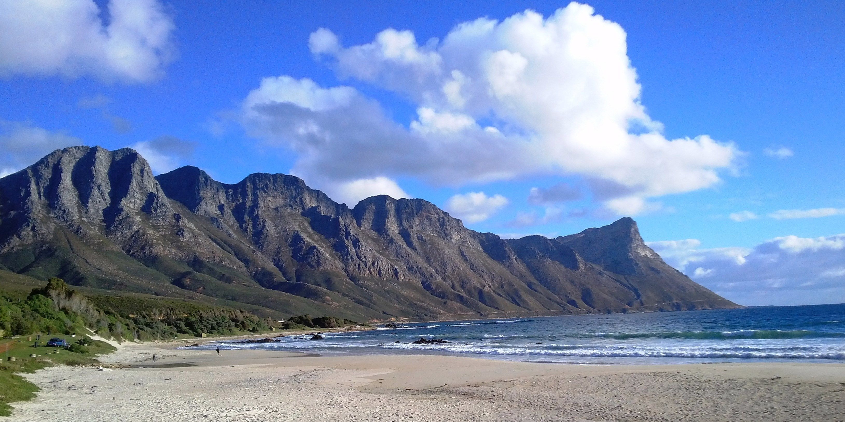 A beach with a mountain backdrop, clear skies, and calm sea.
