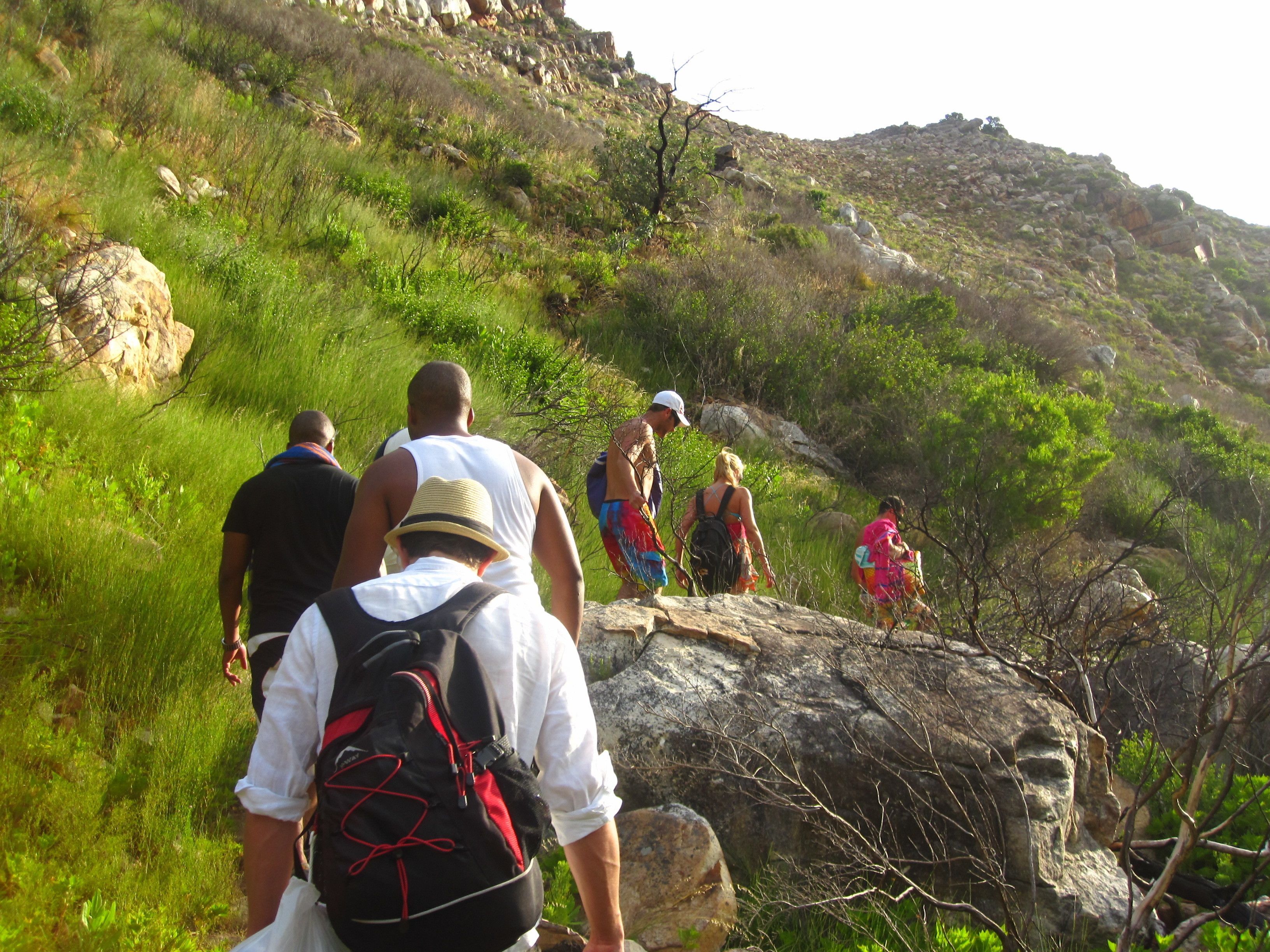 A group of people hiking on a grassy hillside with rocky terrain.