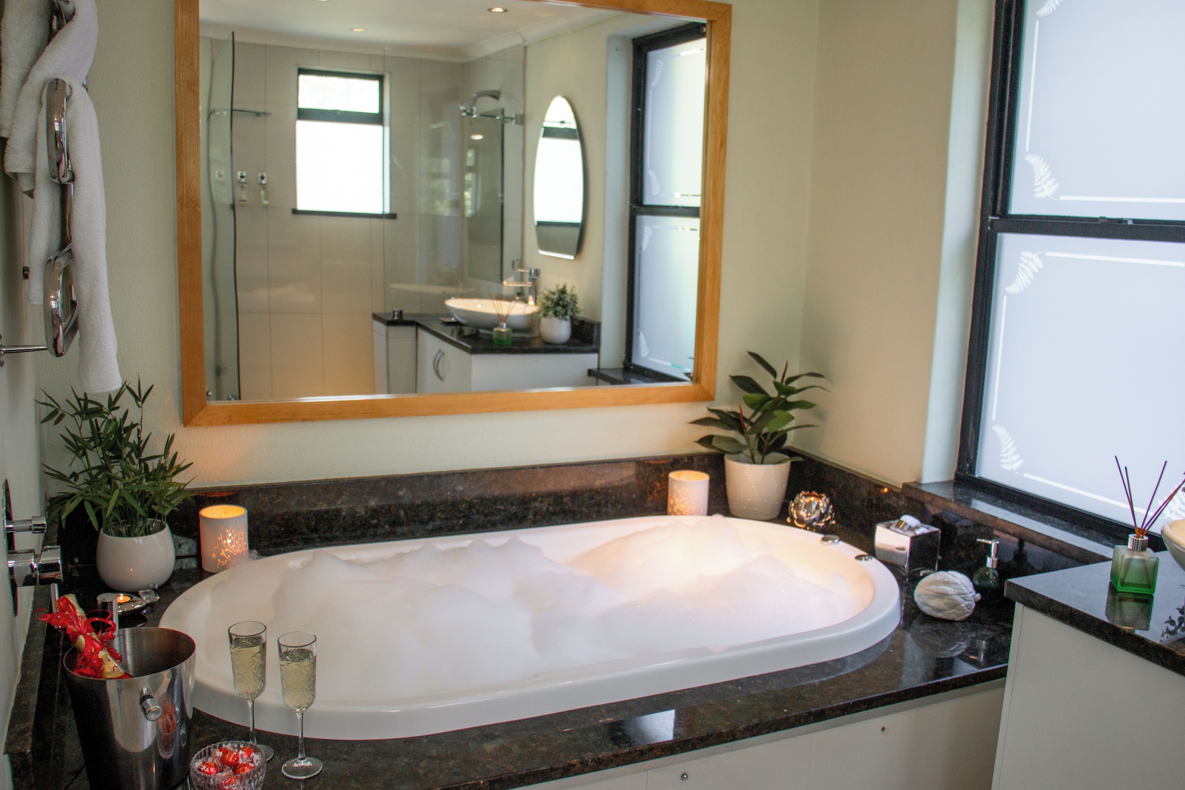 A modern bathroom with a large bathtub, a large mirror, and a window.