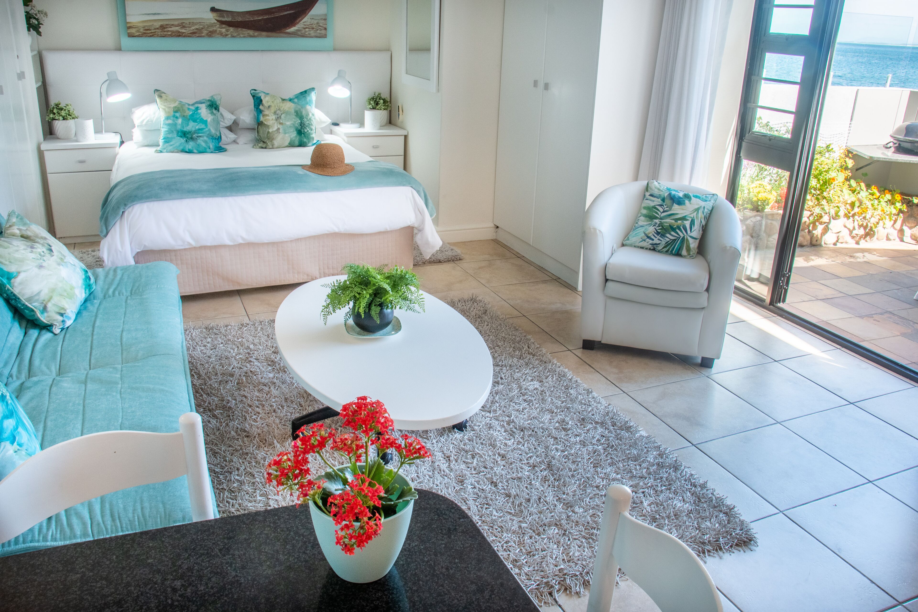 A modern bedroom with a bed, bedside tables, a sofa, a chair, and a dining table with a vase of flowers.