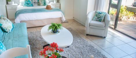 A modern bedroom with a bed, bedside tables, a sofa, a chair, and a dining table with a vase of flowers.