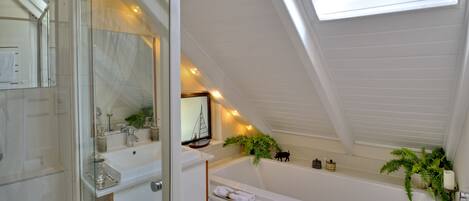 A modern bathroom with a skylight, a bathtub, and a vanity with a mirror.