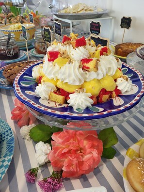 A dessert display with a variety of cakes and pastries, including a cake with whipped cream and fruit toppings, on a decorative plate. - Maree Hotel (Cesenatico)
