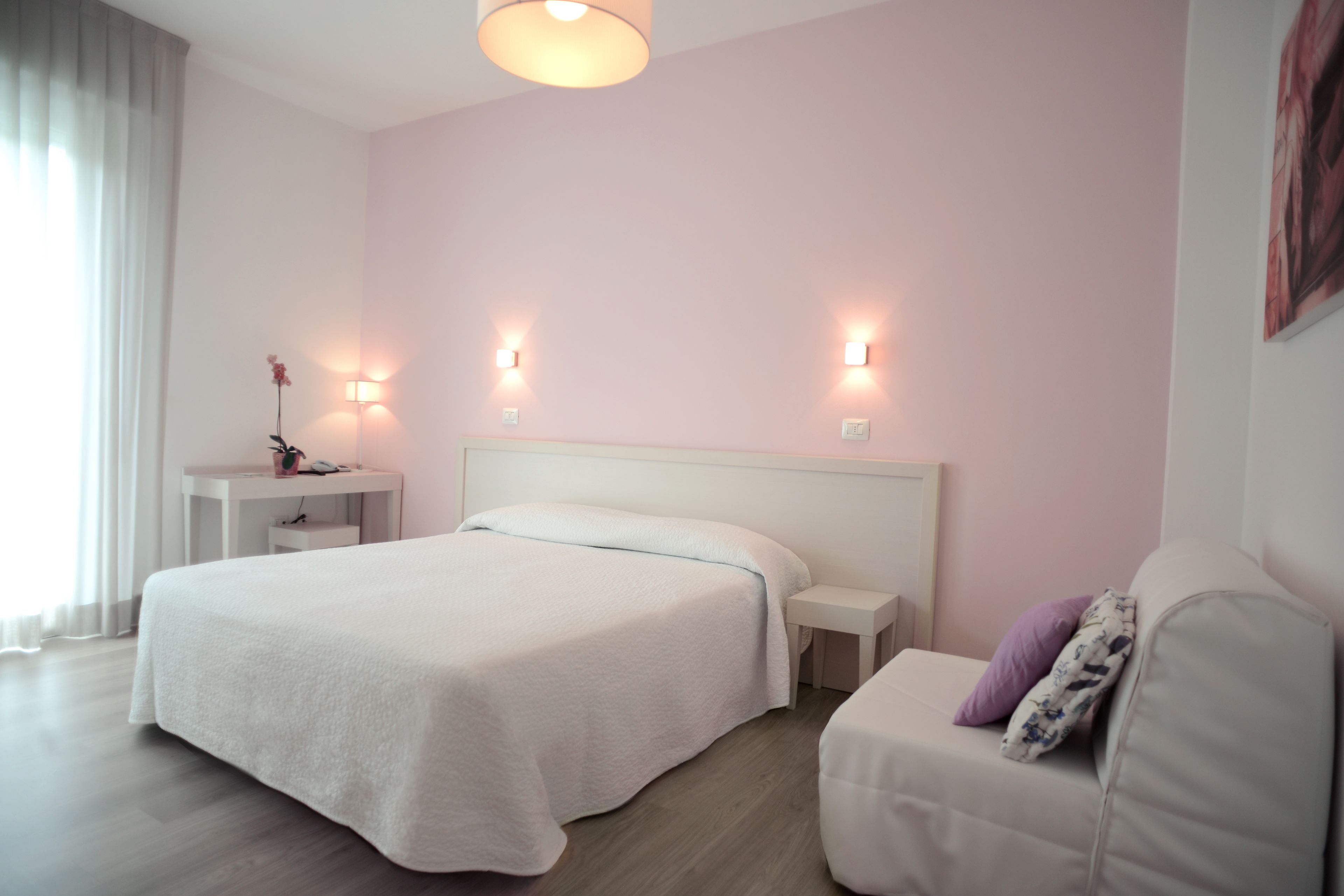 A hotel room with a large bed, bedside tables, a nightstand, a sofa, and wall-mounted lighting.