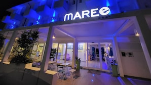 A modern building with a prominent 'MAREE' sign, outdoor seating area, and glass doors leading into the interior. - Maree Hotel (Cesenatico)
