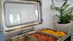 A buffet setup with various food items, a digital clock, and framed artwork on the wall. - Maree Hotel (Cesenatico)
