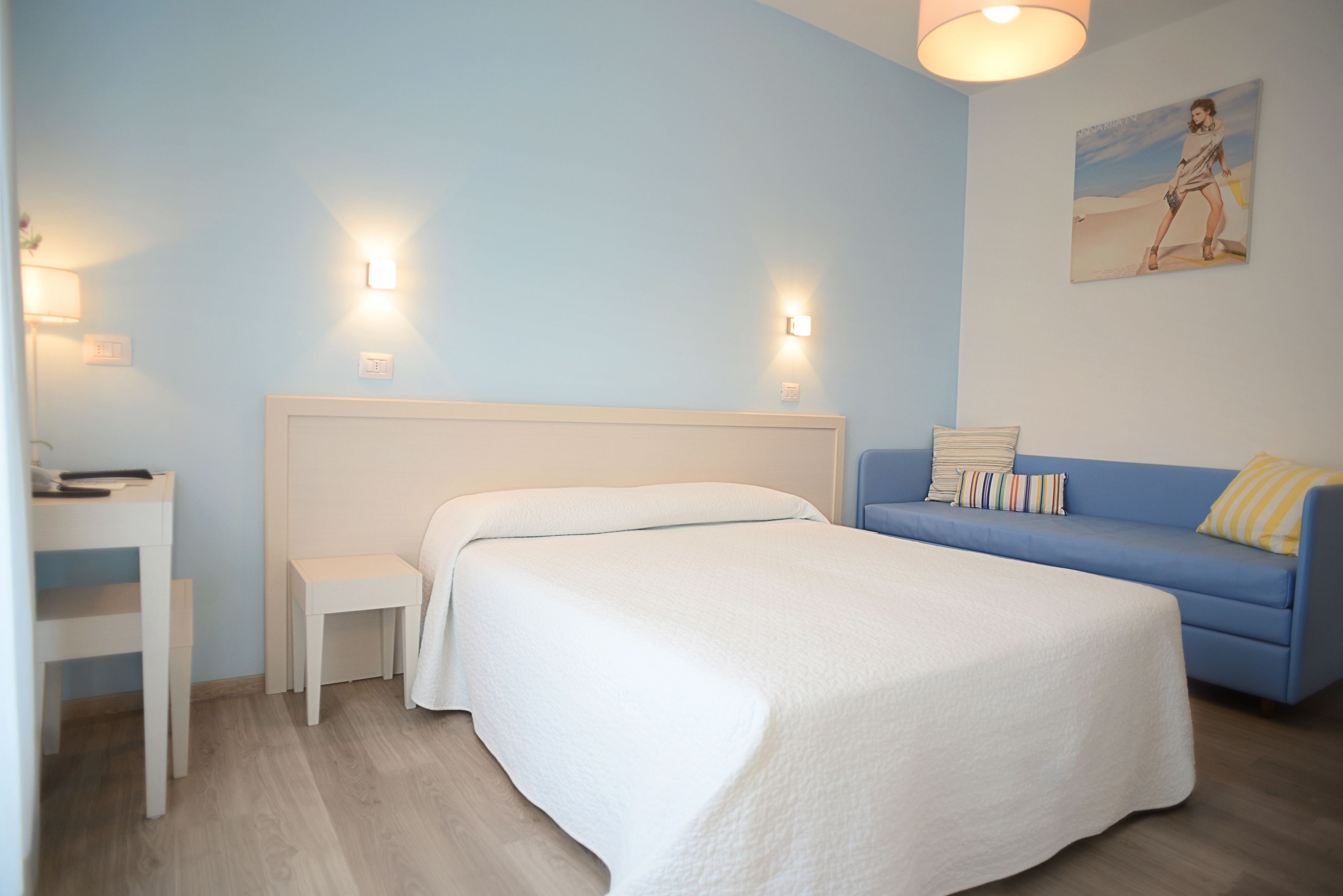 Une chambre à coucher avec un lit, une petite table de chevet, un canapé bleu et une lampe fixée au mur.