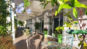 An outdoor seating area with tables and chairs, surrounded by potted plants and greenery. - Maree Hotel (Cesenatico)