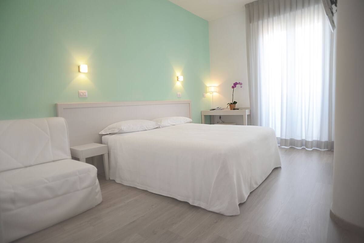 A hotel room with a bed, a nightstand, a lamp, and a window with curtains.