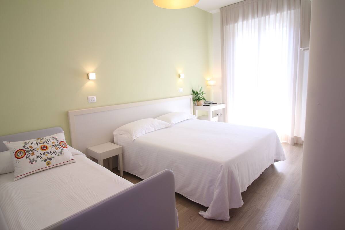 A hotel room with two beds, a nightstand, a lamp, and a potted plant.