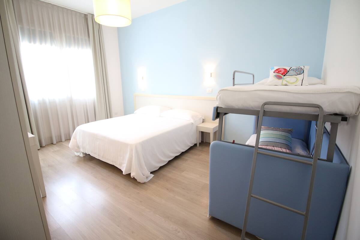 A room with a bunk bed, a single bed, a small table, and a lamp.