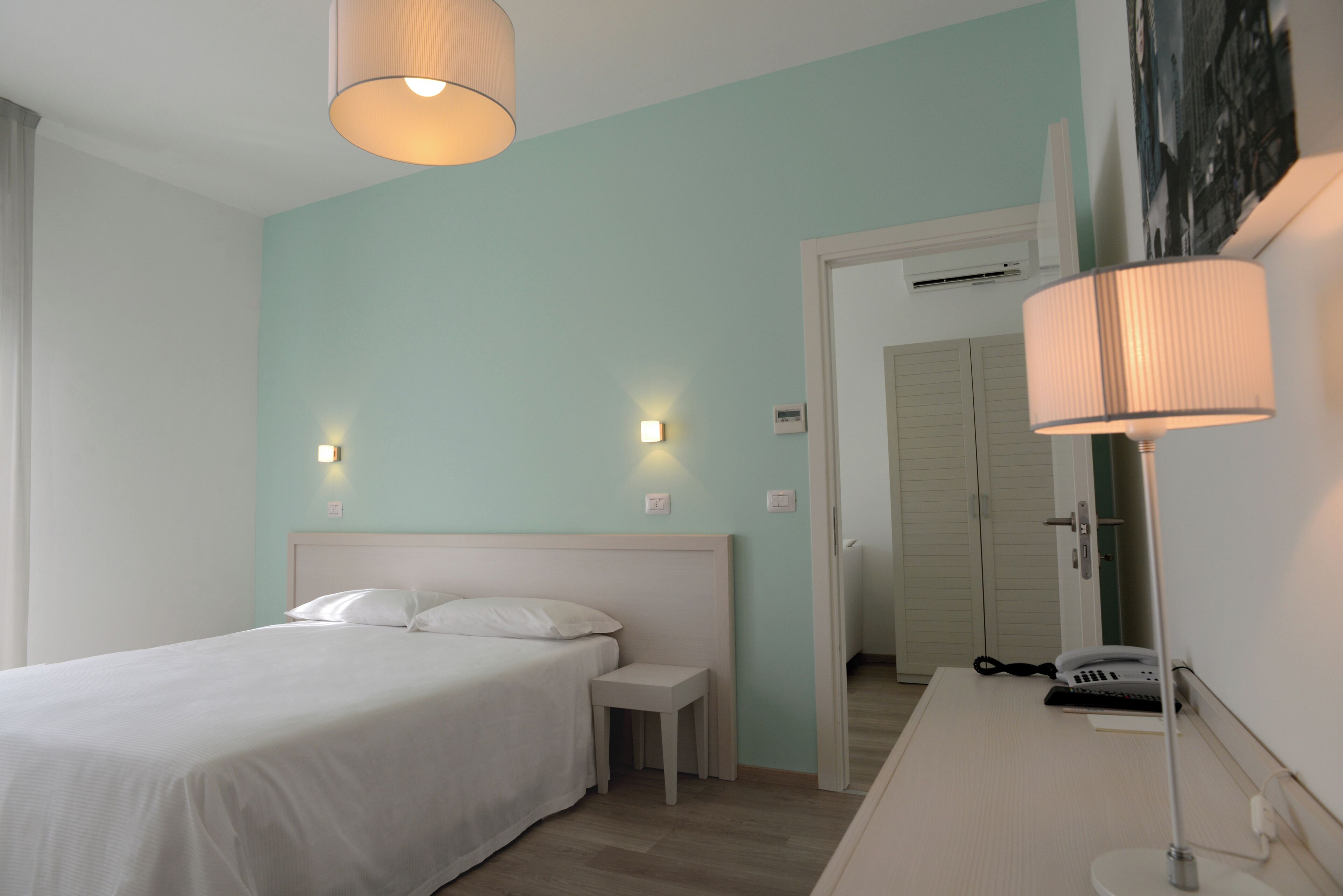Un dormitorio con cama, mesita de noche, lámpara y una puerta que da a otra habitación.