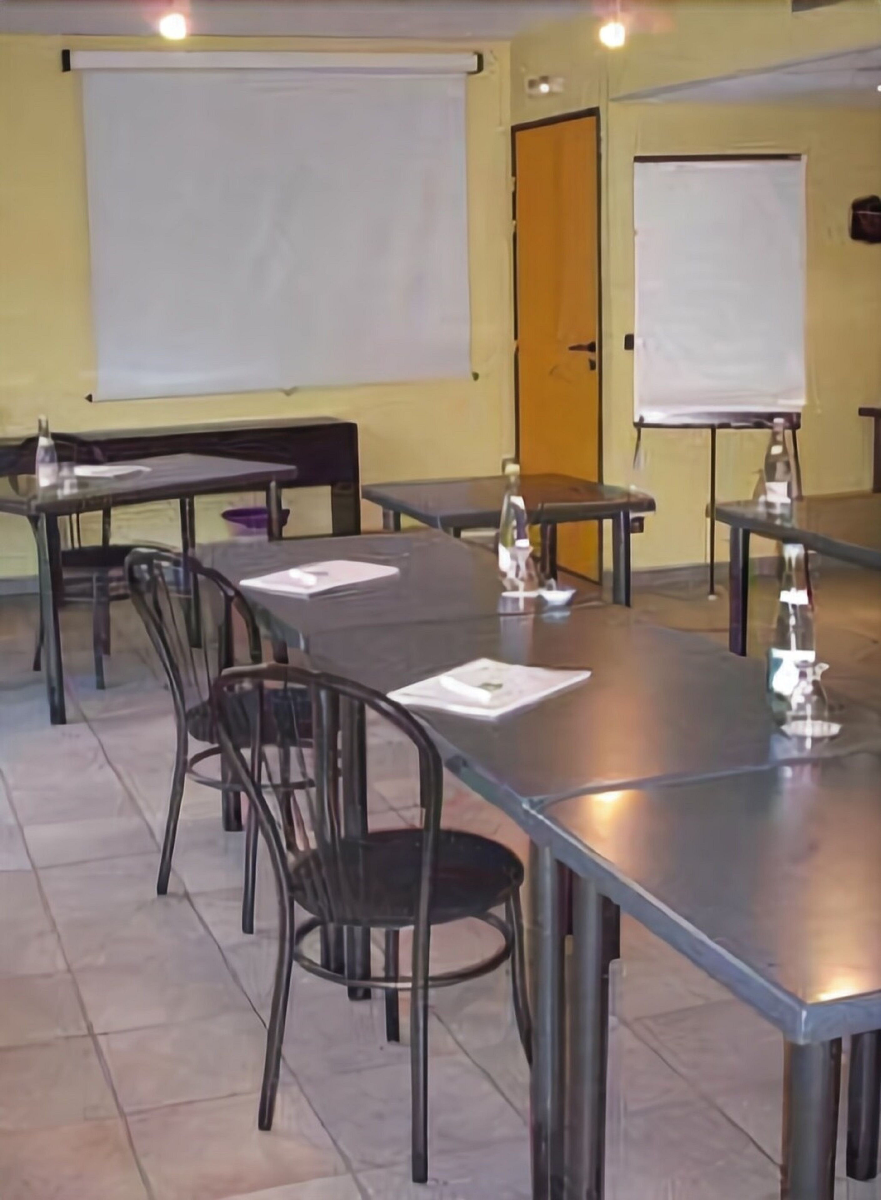 Een vergaderruimte met een grote tafel, stoelen, een projectiescherm en een whiteboard.