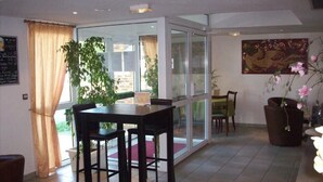A dining area with a table and chairs, a glass partition, and a view of the outside. - Hotel Kimotel (Epone)