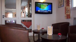 A hotel lobby with leather seating, a television displaying a map, and a small table with a menu. - Hotel Kimotel (Epone)